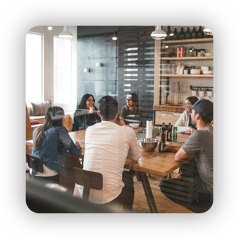 Equipo de trabajo reunido alrededor de una mesa riendo y conversando, representando el ambiente laboral amigable.